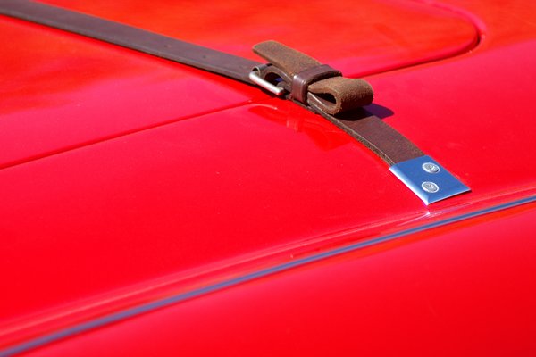 Leather strap on hood: A red classic sportscar with a leather strap to hold the hood/bonnet.