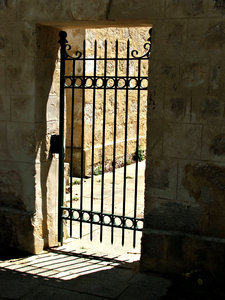 behind iron gates: solid locked stone dark room with iron gate/grill door and brightly lit courtyard