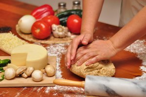 Kneading Pizza dough: Woman kneading whole-wheat Pizza dough on a wooden table, with ingredients in the background