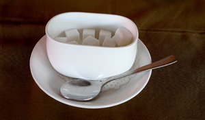 Sugar Pot: A sugar in a white pot or dish on a saucer and a silver spoon beside it.
