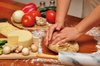 Kneading Pizza dough: Woman kneading whole-wheat Pizza dough on a wooden table, with ingredients in the background