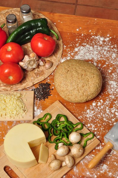 Pizza dough and ingredients: Pizza ingredients and whole-wheat dough on a wooden table sprinkled with flour