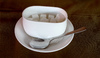 Sugar Pot: A sugar in a white pot or dish on a saucer and a silver spoon beside it.