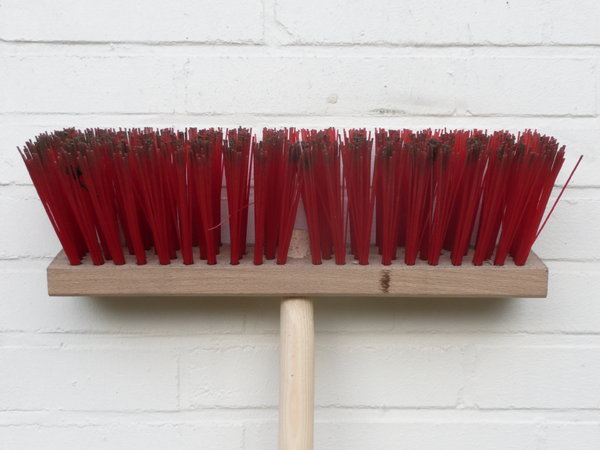 Broom: Broom with red bristles leaning against a white wall