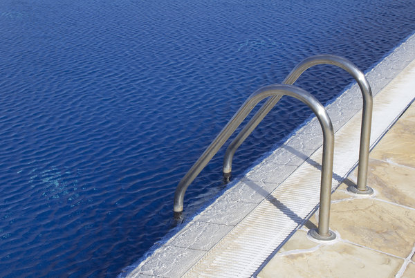 Swimming pool handrail: Handrail and steps into a large outdoor swimming pool.