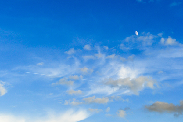 Blue sky with clouds and moon: A plane crossing the blue sky and in the background you can see the moon.