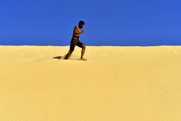 running on a Desert Dune: Fitness model is running on desert dunes for practice, for good health and to maintain his perfect body. Sand and sky only in the photo and the young adult is having a great time and enjoying his life.