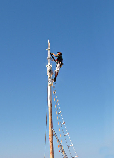 up the mast: workman - rigger doing renovating and maintenance work on pearling lugger's mast