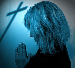 Easter Prayer 2 Duotone: A woman praying, with the shadow of a cross in the background. Blue tones, special light.